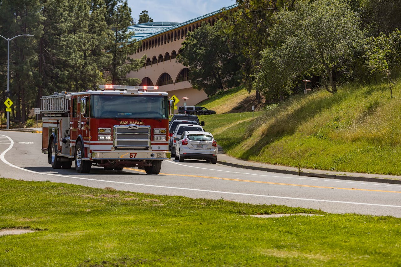 hero-img-02 A San Rafael fire truck driving along a sunny road with green surroundings in California.