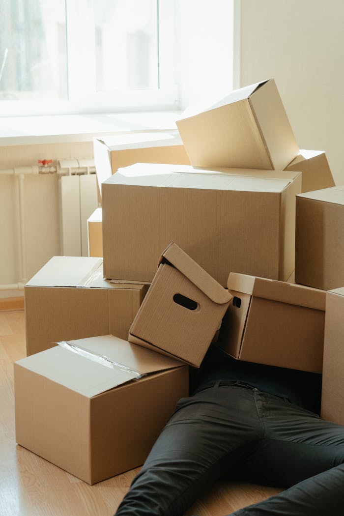 why-choose-us A person buried under a pile of cardboard boxes during a home move, depicting exhaustion.