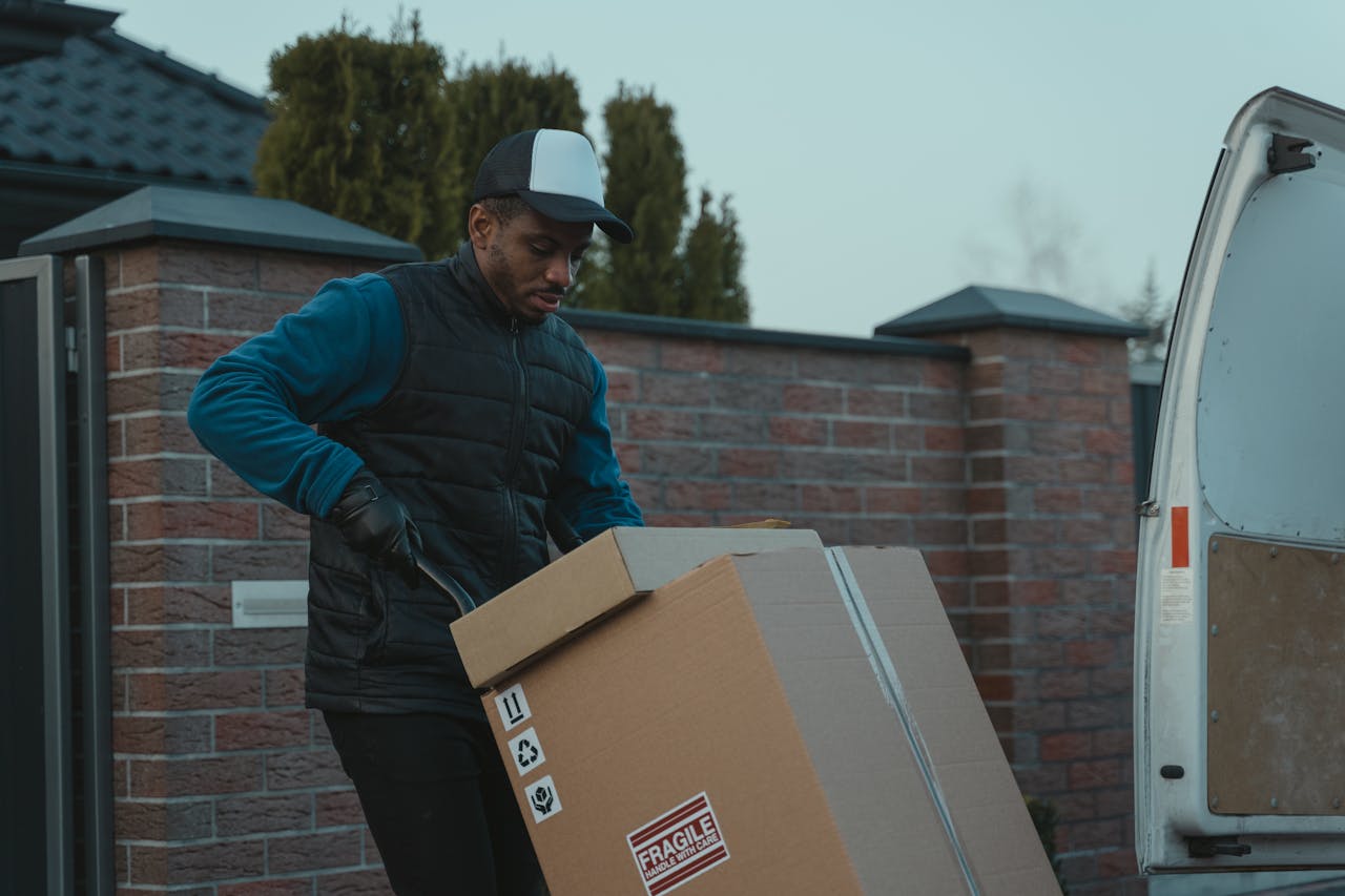 Courier loading cardboard box into a van outdoors, showcasing logistics work.