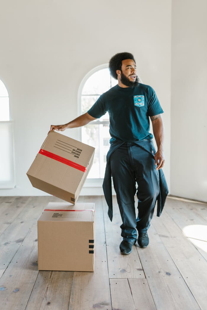 A mover carefully handles boxes in a bright, empty room on moving day.